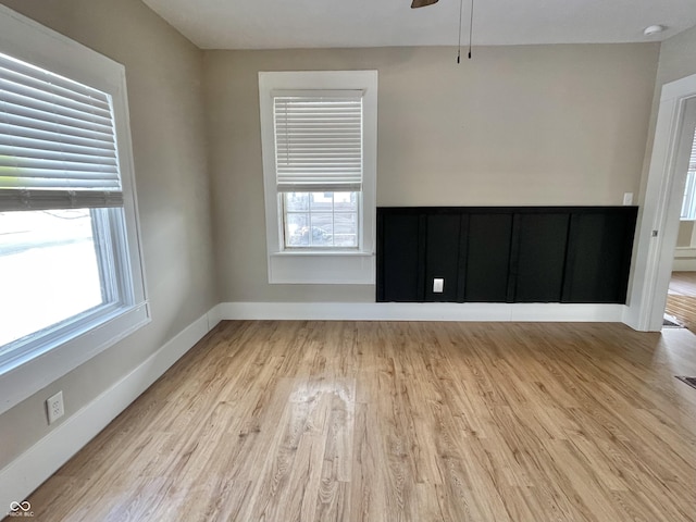 empty room featuring baseboards, plenty of natural light, light wood finished floors, and ceiling fan