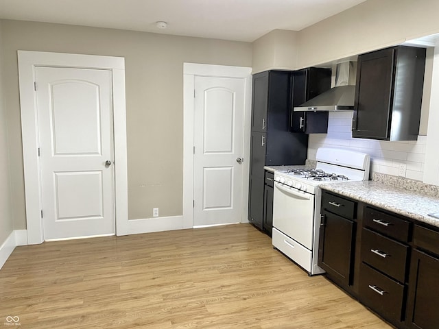 kitchen with light wood finished floors, white range with gas stovetop, decorative backsplash, light countertops, and wall chimney range hood