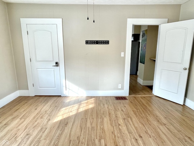 empty room featuring light wood-type flooring, visible vents, and baseboards