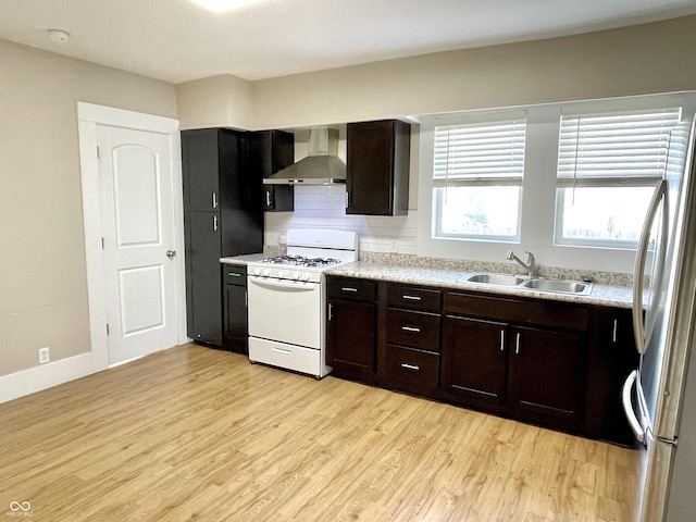 kitchen featuring white gas range oven, wall chimney exhaust hood, light countertops, light wood-type flooring, and a sink