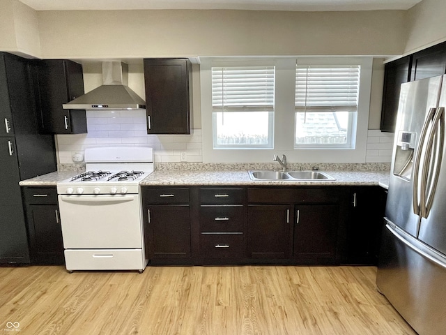 kitchen with stainless steel fridge, white gas range oven, light countertops, wall chimney range hood, and a sink