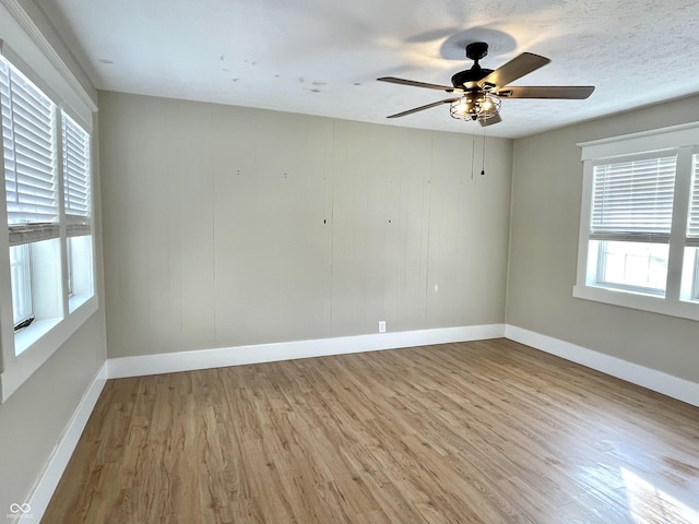 empty room with a textured ceiling, ceiling fan, light wood-type flooring, and baseboards