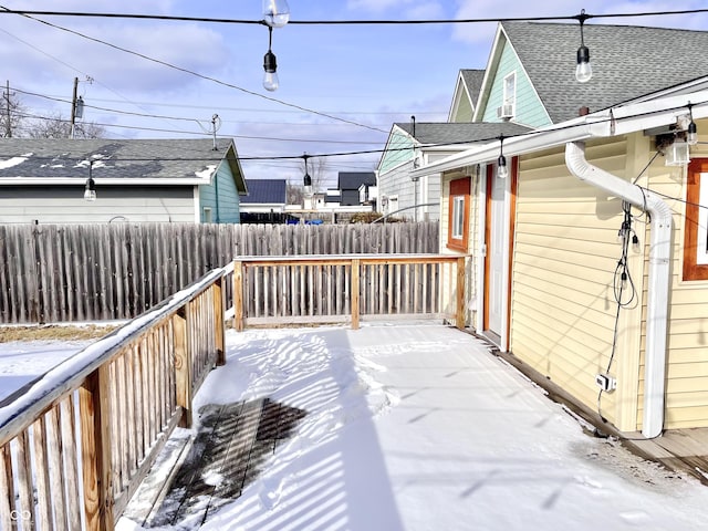 snow covered deck with a fenced backyard