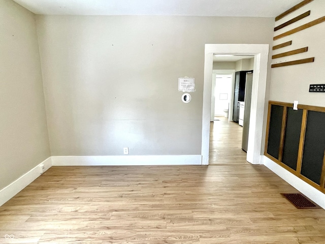 empty room with light wood-style flooring, visible vents, and baseboards