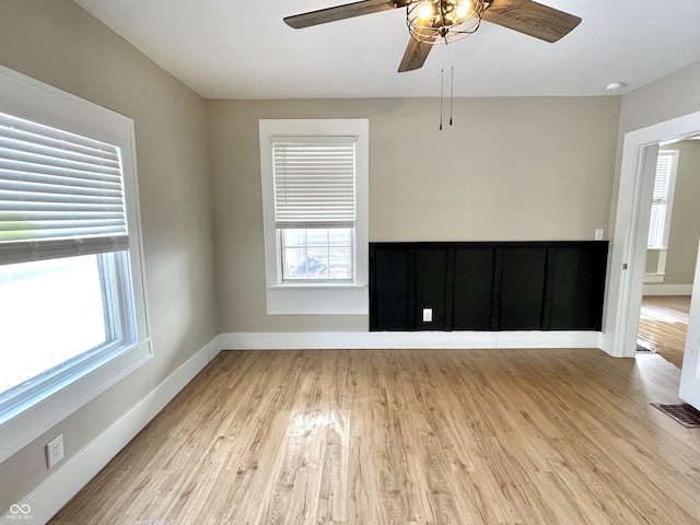 empty room with ceiling fan, light wood-type flooring, visible vents, and baseboards