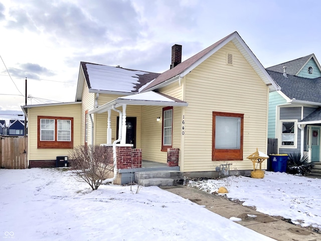 view of front of home with a chimney, a porch, and central AC