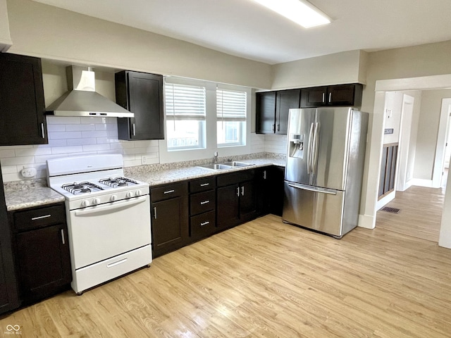 kitchen with light wood-style floors, white range with gas cooktop, light countertops, wall chimney exhaust hood, and stainless steel fridge