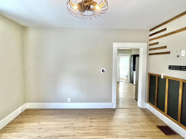 spare room with light wood-type flooring, visible vents, a notable chandelier, and baseboards