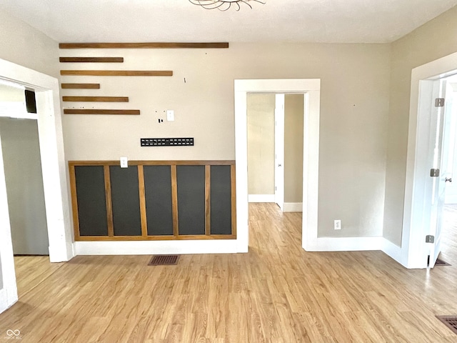 empty room with light wood finished floors, baseboards, and visible vents