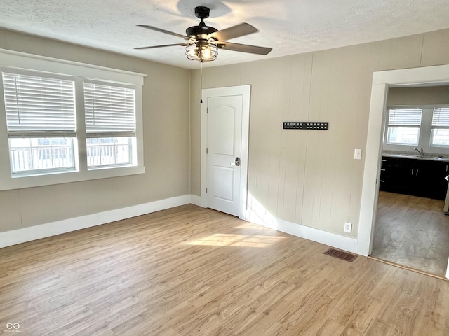 spare room featuring light wood-type flooring, visible vents, a sink, and a textured ceiling