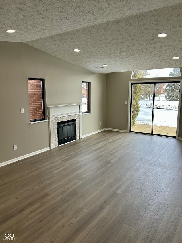 unfurnished living room featuring baseboards, a tiled fireplace, wood finished floors, vaulted ceiling, and a textured ceiling