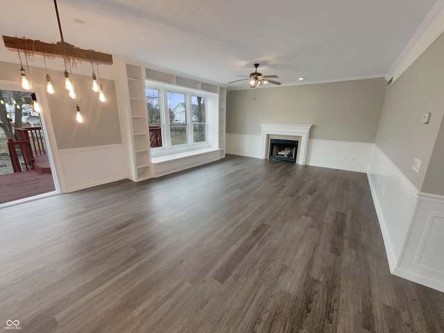 unfurnished living room featuring built in features, dark wood-style floors, ceiling fan, crown molding, and a fireplace