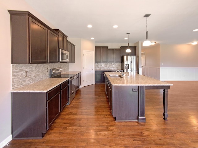 kitchen featuring a center island with sink, hanging light fixtures, stainless steel appliances, dark hardwood / wood-style flooring, and sink