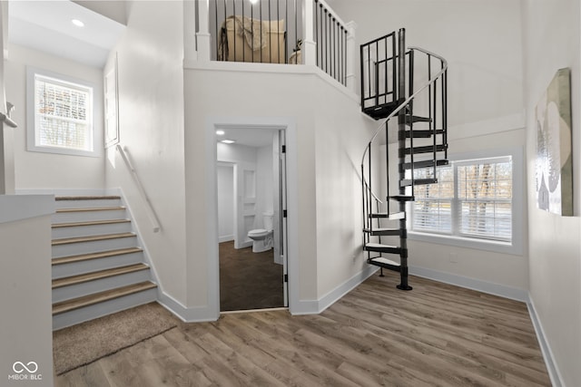 stairs with recessed lighting, wood finished floors, a towering ceiling, and baseboards