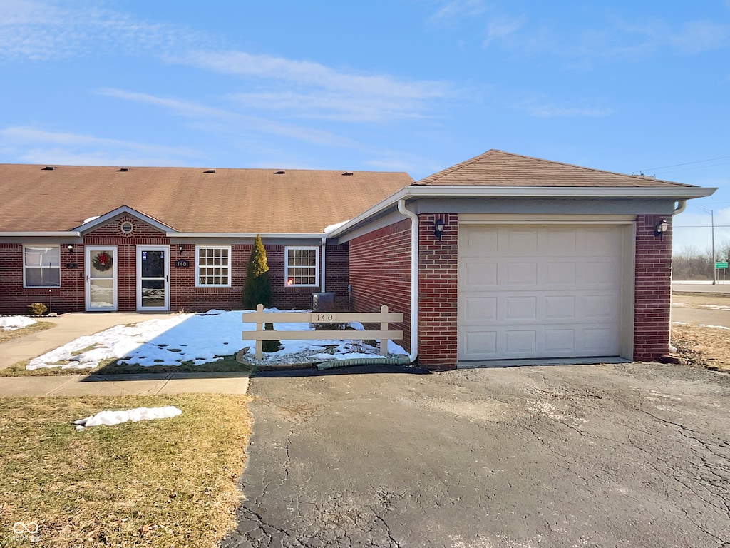 view of front of house with an attached garage, brick siding, fence, driveway, and roof with shingles