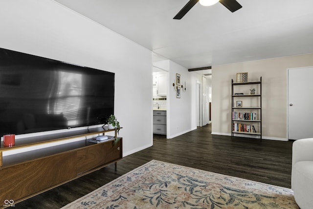 living area featuring baseboards, dark wood-type flooring, and a ceiling fan