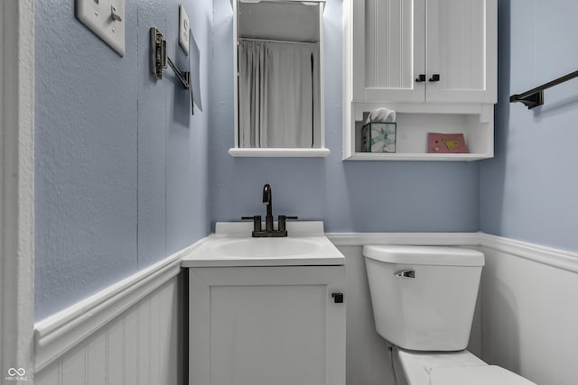 bathroom with toilet, vanity, and wainscoting