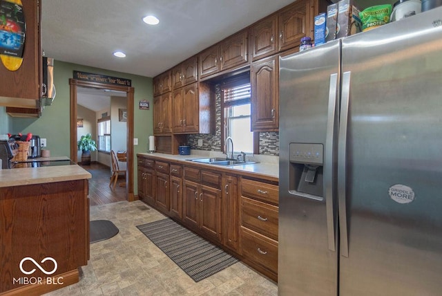 kitchen with stainless steel fridge, range, decorative backsplash, light countertops, and a sink