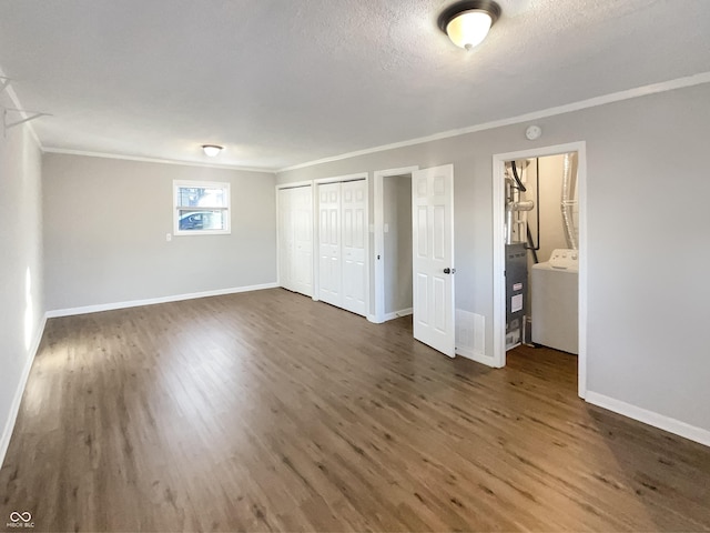 unfurnished bedroom featuring two closets, washer / clothes dryer, dark wood-type flooring, ornamental molding, and baseboards