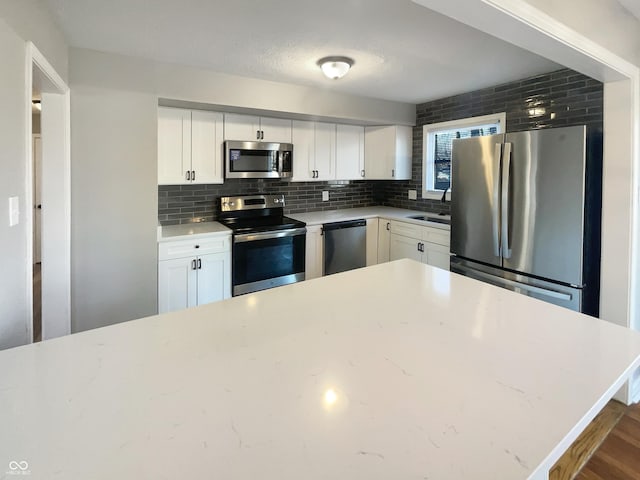 kitchen featuring tasteful backsplash, light countertops, appliances with stainless steel finishes, white cabinetry, and a sink