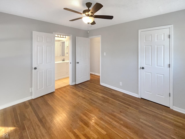 unfurnished bedroom with a ceiling fan, ensuite bathroom, baseboards, and wood finished floors