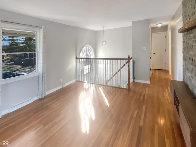 unfurnished room featuring baseboard heating, wood finished floors, and baseboards