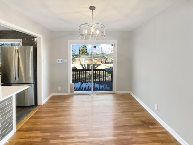 unfurnished dining area with baseboards, wood finished floors, visible vents, and a notable chandelier