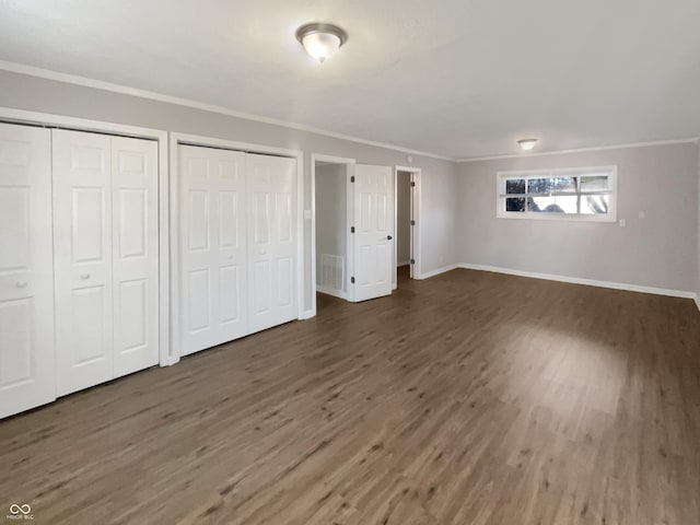 unfurnished bedroom with dark wood-style floors, baseboards, ornamental molding, and multiple closets