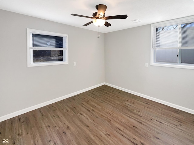 unfurnished room with dark wood-style flooring, a ceiling fan, and baseboards