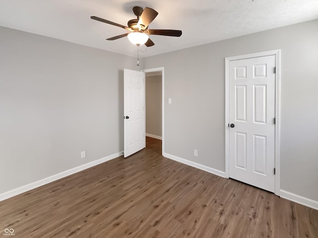 unfurnished bedroom featuring dark wood-type flooring, a textured ceiling, baseboards, and a ceiling fan