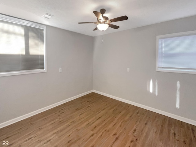 spare room with a ceiling fan, visible vents, baseboards, and wood finished floors