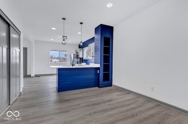 kitchen with light wood-type flooring, white cabinets, decorative light fixtures, sink, and kitchen peninsula