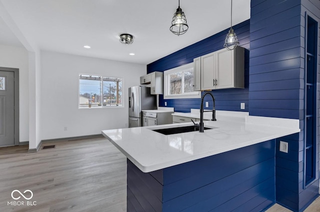 kitchen featuring sink, stainless steel refrigerator with ice dispenser, pendant lighting, kitchen peninsula, and white cabinets