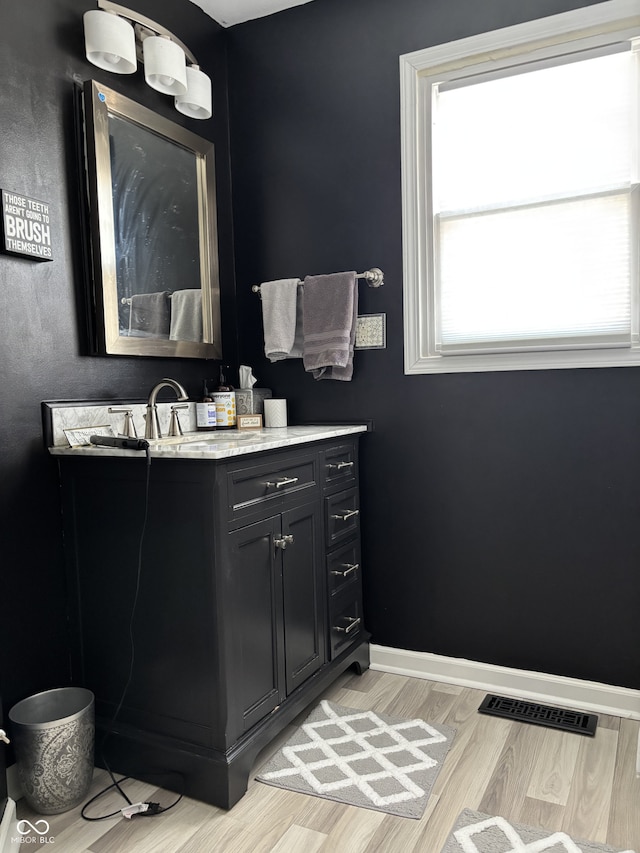 bathroom with visible vents, vanity, baseboards, and wood finished floors