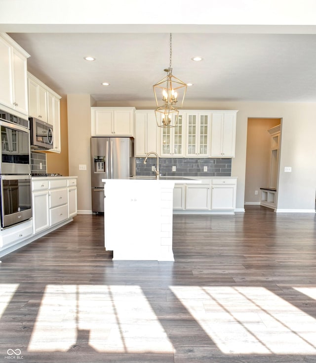 kitchen featuring glass insert cabinets, stainless steel appliances, light countertops, a center island with sink, and pendant lighting