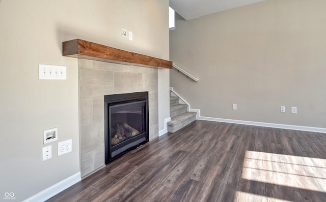 unfurnished living room with dark wood-type flooring, a fireplace, baseboards, and stairs