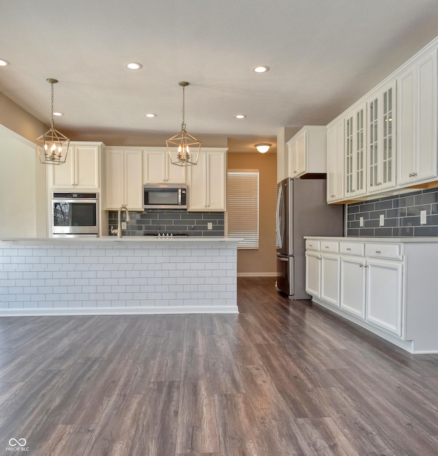 kitchen featuring dark wood finished floors, glass insert cabinets, hanging light fixtures, stainless steel appliances, and white cabinetry