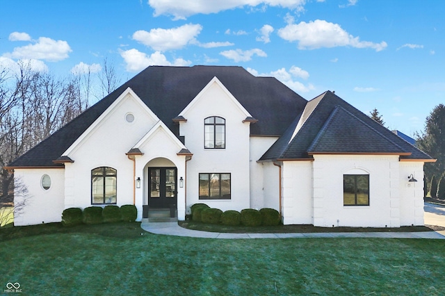 french country inspired facade with a shingled roof, french doors, and a front lawn