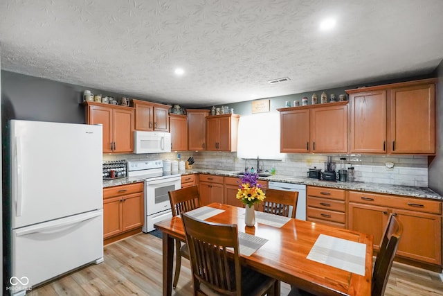 kitchen featuring white appliances, a sink, light wood finished floors, and light stone countertops