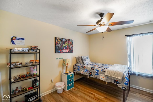 bedroom with ceiling fan, a textured ceiling, baseboards, and wood finished floors