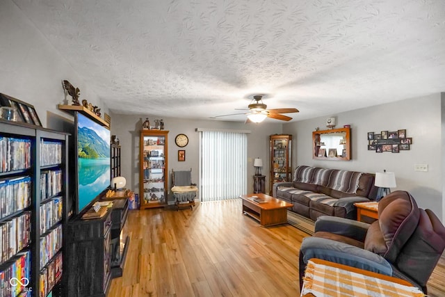 living area with a textured ceiling, ceiling fan, and light wood-type flooring