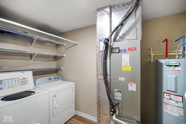 laundry area with light wood-style flooring, electric water heater, separate washer and dryer, laundry area, and baseboards