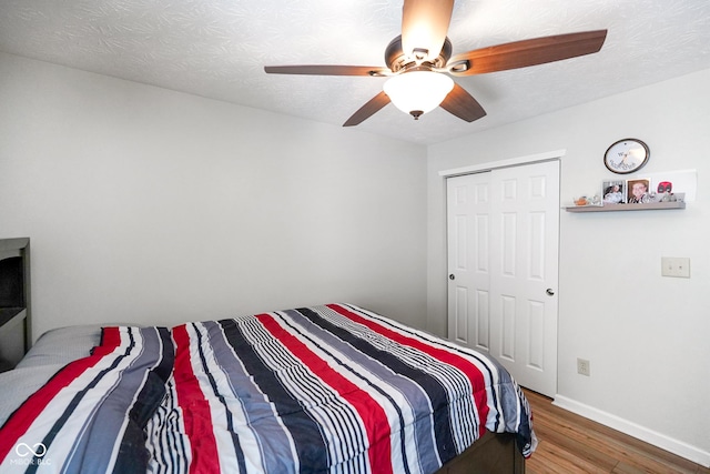 bedroom featuring a textured ceiling, ceiling fan, wood finished floors, baseboards, and a closet