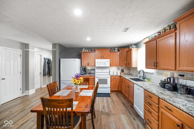 kitchen with white appliances, visible vents, light stone countertops, light wood-style floors, and a sink