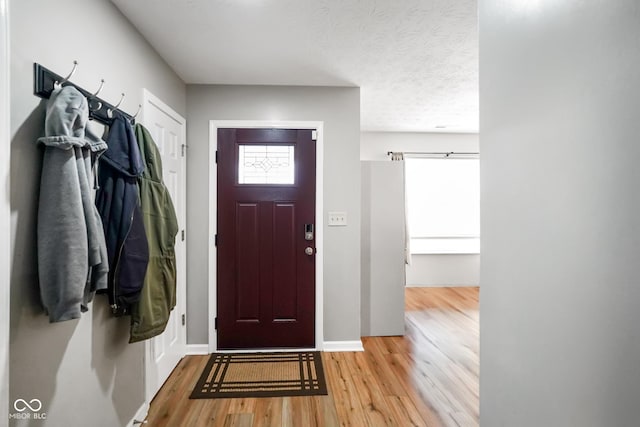 foyer entrance with a textured ceiling, light wood finished floors, and baseboards