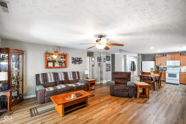 living room with a ceiling fan, light wood-type flooring, visible vents, and baseboards