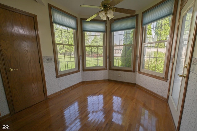 unfurnished sunroom featuring wallpapered walls, plenty of natural light, and wood finished floors