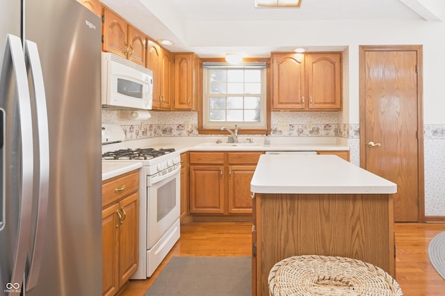 kitchen featuring a sink, light wood-style floors, white appliances, light countertops, and a center island