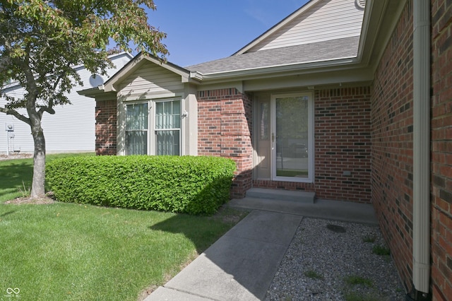 view of exterior entry with a yard and brick siding