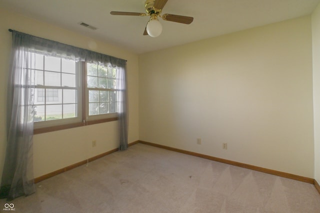 spare room with light colored carpet, baseboards, visible vents, and ceiling fan